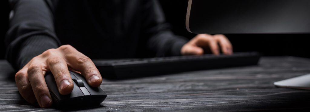 Person using computer with focus on mouse and keyboard, representing the importance of cybersecurity and compliance with UK government legislation.