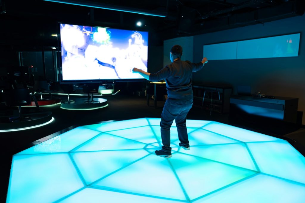 Person interacting with immersive AV installation using illuminated digital floor and large projection screen.