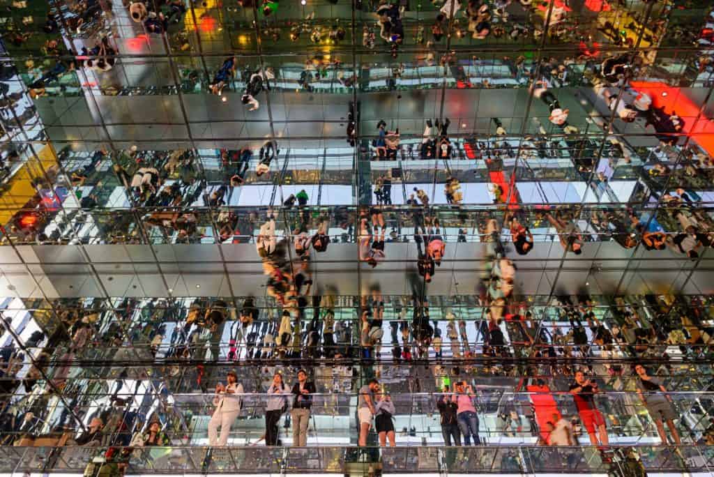 Crowd of people reflected in mirrored surfaces, symbolising the impact of overcrowded networks on WiFi performance in busy commercial environments.