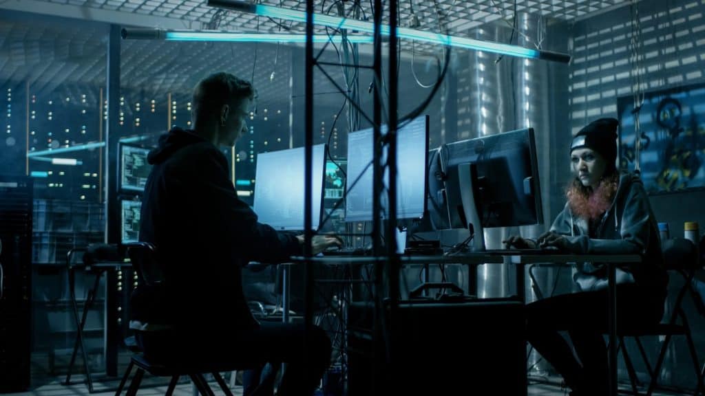 Two individuals in a dark room working on computers, symbolising potential WiFi security risks and cyber threats in commercial network environments.
